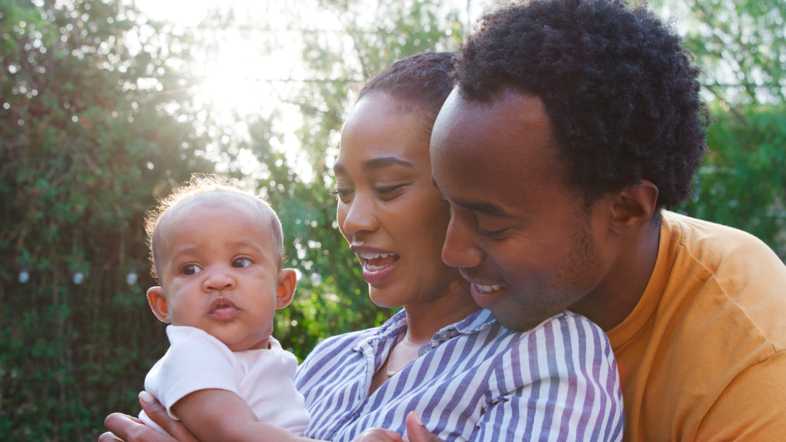 Loving Parents Holding Baby Daughter At Home Outdoors In Garden